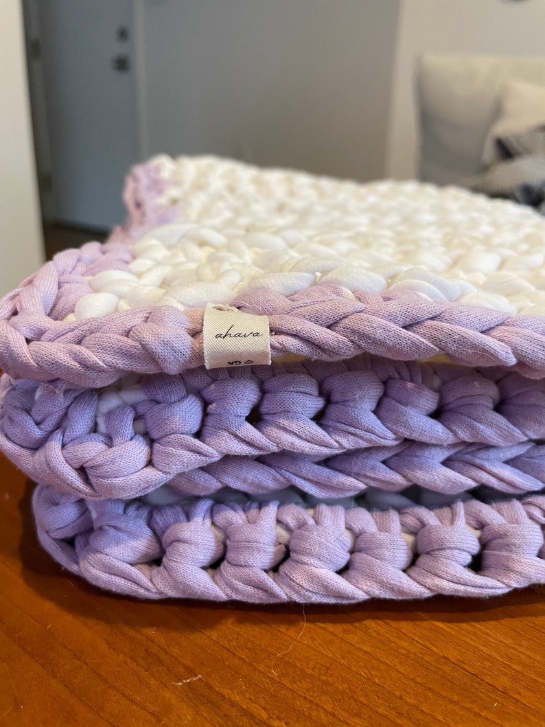 Puede incluir: Un primer plano de una alfombra de crochet de color morado y blanco con una etiqueta que dice "ahava".