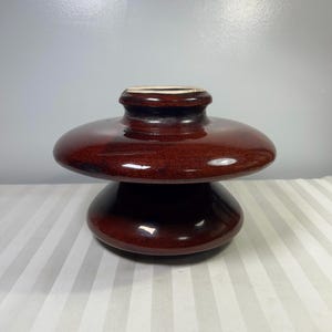 Peut inclure: Un isolateur en céramique marron avec une finition brillante. L'isolateur a une conception empilée en forme de disque, avec une petite section supérieure et une base plus large. La surface reflète la lumière, soulignant sa texture lisse. L'objet est probablement utilisé dans les applications électriques.