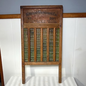 Puede incluir: Un antiguo lavadero de madera con el texto "National Washboard Co." y "801". El lavadero tiene un marco de madera con una superficie de fregado de metal corrugado y listones de madera. Hecho en los EE. UU.