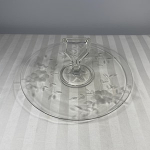 以下が含まれることがあります： ハンドル付きの透明なガラス製サービングトレイ。トレイの縁にはエッチングされた花の模様があります。ハンドルは無垢のガラスです。トレイは丸く、台座の上にあります。