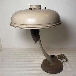 May include: A vintage desk lamp with a beige metal shade and a brown metal base. The lamp has a flexible arm and a cord.
