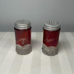 Puede incluir: Un par de saleros y pimenteros vintage. Los saleros son de vidrio rojo rubí con tapas de metal plateado. El nombre "George" está grabado en un salero y "Marian" en el otro. Las bases son de vidrio transparente texturizado.