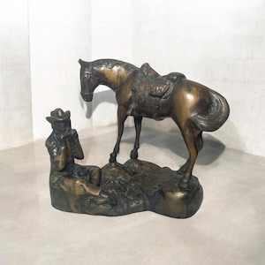 May include: A bronze sculpture of a cowboy playing a harmonica while sitting next to a horse with a saddle.