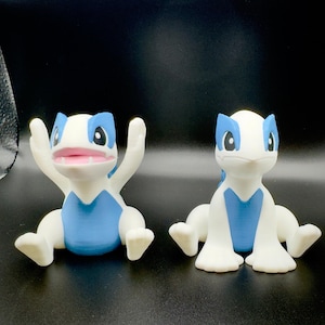 May include: Two white and blue figurines of a cartoon lizard-like creature. One figurine has its arms raised, mouth open, and the other is in a seated position. The figurines have blue accents and pink mouths.