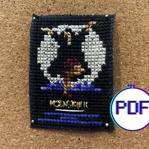 May include: A cross-stitch pattern featuring a black and white image of a person standing on a blue platform. The text "MONOCHROM" is visible at the bottom of the pattern.