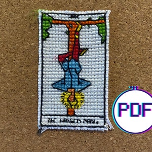 Könnte beinhalten: Ein Kreuzstichmuster der Tarotkarte Der Gehängte. Die Karte ist weiß mit einem bunten Bild einer Person, die kopfüber an einem Baum hängt. Der Text "THE HANGED MAN" befindet sich am unteren Rand der Karte.