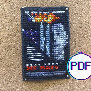 May include: A cross-stitch pattern featuring a black and white image of a person with a flower on their head. The pattern is titled "Die More".