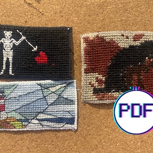 May include: Three small cross-stitch embroidery pieces on a corkboard. The first piece is a black flag with a white skeleton holding a sword and a red heart. The second piece is a red and brown cross-stitch of a black dog. The third piece is a blue and white cross-stitch of a lighthouse on a green shore.