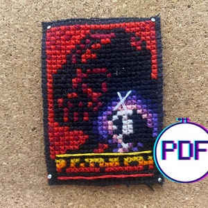 May include: A cross-stitch pattern of a purple and pink character with a white outline, set against a black background with red and yellow accents. The pattern is framed with black thread and has a "PDF" label in the bottom right corner.