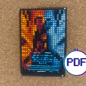 May include: A cross-stitch pattern with a fiery orange and red design on the left side and a blue and teal design on the right side. The pattern is framed with black thread and is mounted on a corkboard.