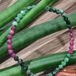 Op de afbeelding: Een groene, zwarte en roze edelsteen armband met kleine, gefacetteerde kralen. De armband is gemaakt van natuurlijke stenen en is een prachtig voorbeeld van handgemaakte sieraden.