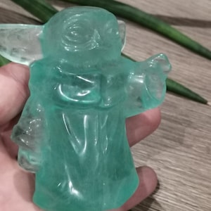 Peut inclure: Une figurine translucide verte d'un personnage de la franchise Star Wars. La figurine est en position debout, un bras levé.