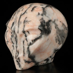 Peut inclure: Un crâne d'alien sculpté en marbre rose et noir. Le crâne a un visage détaillé avec des yeux, un nez et une bouche.