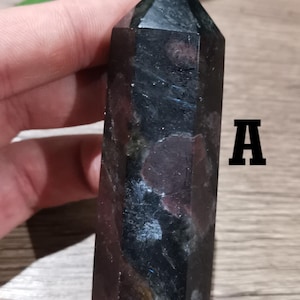 Peut inclure: Pointe de cristal noire et rouge avec une pointe pointue et une forme facetée. Le cristal mesure environ 5 cm de long et a une base foncée, presque noire, avec des inclusions rouges et blanches.