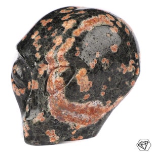 Peut inclure: Une sculpture en pierre sculptée représentant une tête d'extraterrestre. La sculpture est principalement vert foncé avec des taches brun-rouge et une surface lisse et polie. La tête d'extraterrestre a de grands yeux et une structure faciale définie.