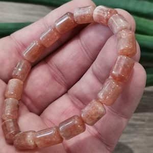May include: A bracelet made of orange sunstone beads. The beads are rectangular and have a slightly translucent appearance.