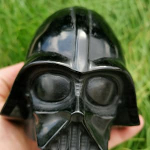 May include: A black obsidian Darth Vader sculpture. The sculpture is detailed and features the iconic helmet, mask, and breathing apparatus.