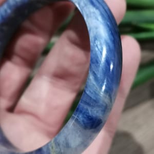 May include: A blue and white marbled bangle bracelet. The bracelet is a solid, circular band with a polished, glossy finish. The color is a deep blue with white marbling throughout. The bracelet is held in a hand.