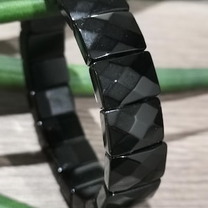 May include: A black bracelet made of faceted obsidian beads. The beads are arranged in a staggered pattern, creating a unique and stylish look.