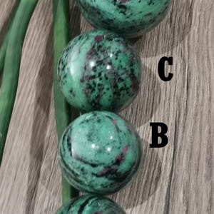 Op de afbeelding: Vier groene en zwarte edelsteenkogels, gelabeld A, B, C en D, verticaal gerangschikt op een houten oppervlak.