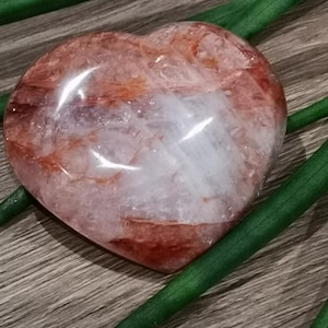 Peut inclure: Un cristal en forme de cœur avec un centre blanc clair et des tourbillons rouges et orange. Le cristal repose sur une surface en bois avec des feuilles vertes.