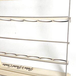 May include: Wooden paint organizer with three shelves and a base. Each shelf has six circular cutouts for holding paint bottles. The base is engraved with the text "Peter's Paint Center".