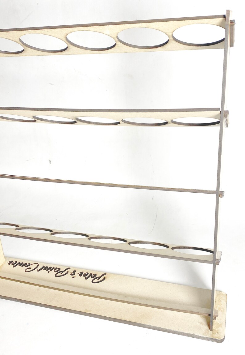 May include: Wooden paint organizer with three shelves and a base. Each shelf has six circular cutouts for holding paint bottles. The base is engraved with the text "Peter's Paint Center".