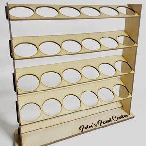 May include: Wooden paint rack with five shelves and 24 circular cutouts for holding paint bottles. The rack has the words "Peter's Paint Center" engraved on the bottom.