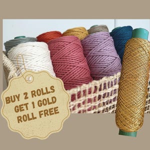 May include: A selection of colourful macrame cord rolls in a woven basket, with a gold roll on the right. The rolls are in shades of white, pink, red, purple, yellow, and teal. The image includes text that says "BUY 2 ROLLS GET 1 GOLD ROLL FREE."