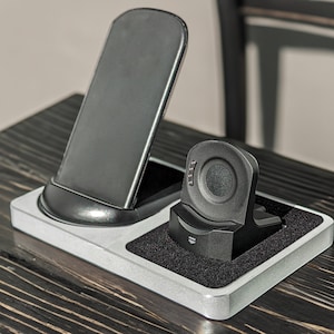 May include: A white charging station with a black phone stand and a black smartwatch stand. The phone stand is angled and the smartwatch stand is circular.