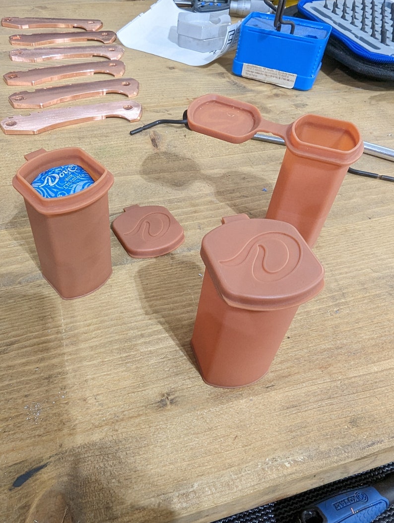 May include: Three brown silicone containers with lids. The containers are cylindrical and have a wave design on the lids. One container has a blue lid with a white design.