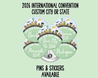 Może przedstawiać: Pięć okrągłych przypinek z jasnym zielonym tłem, ilustracją panoramy miasta z balonem na ogrzane powietrze oraz tekstem 2026 INTERNATIONAL CONVENTION CUSTOM CITY OR STATE. Każda przypinka zawiera napis LOVE FROM YOUR FAMILY IN oraz nazwy lokalizacji.