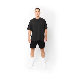 Könnte beinhalten: Eine Person trägt ein schwarzes, übergroßes T-Shirt und schwarze Shorts. Das T-Shirt hat kurze Ärmel und einen Rundhalsausschnitt. Die Shorts haben einen Kordelzug in der Taille. Die Person trägt weiße Socken und weiße Turnschuhe.