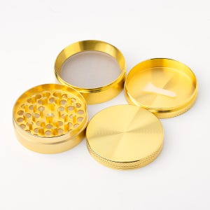 May include: Four piece gold metal grinder with a screen and a small scraper. The grinder has a textured surface.