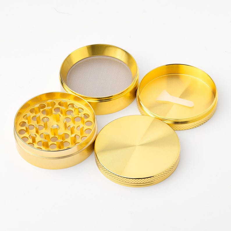 May include: Four piece gold metal grinder with a screen and a small scraper. The grinder has a textured surface.