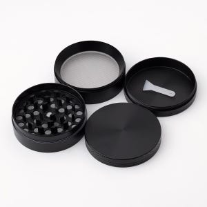 May include: A four-piece black metal grinder with a screen and a scraper. The grinder has a textured surface and a smooth, flat top.