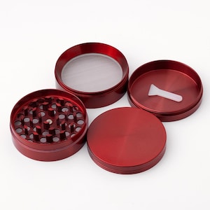 May include: Four piece red metal grinder with a screen and a small plastic scraper.