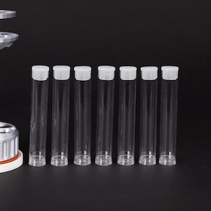 May include: Seven clear, cylindrical vials with white caps are arranged in a row against a black background. The vials are made of transparent plastic. The caps are flat and opaque. Each vial is approximately 10 cm in length.
