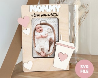 Op de afbeelding: Een houten fotolijst met een foto van een baby en de tekst "MOMMY i love you a latte!" De lijst heeft een roze koffiebeker met een hart erop en roze en witte hartjes rond de foto.