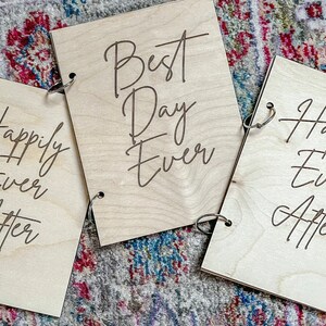Może przedstawiać: Trzy drewniane tabliczki z wygrawerowanym tekstem "Happily Ever After", "Best Day Ever" i "Happily Ever After". Tabliczki są połączone metalowymi k&oacute;łkami.