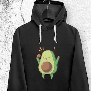 Könnte beinhalten: Schwarzer Hoodie mit einem Cartoon-Avocado, der ein Mikrofon hält und lächelt. Die Avocado ist grün mit einem braunen Kern. Der Text "!" erscheint über der Avocado.