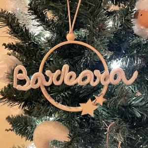 Può includere: Un ornamento in crochet bianco con la parola "Barcelona" appeso a un albero di Natale. L'ornamento è attaccato a un cerchio di legno con due stelle dorate.