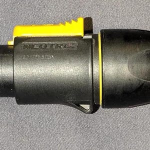 May include: A black and yellow Neutrik connector, likely for audio or video equipment. The connector has a cylindrical shape with a yellow locking mechanism and end cap. The word "NEUTRIK" is printed on the side.