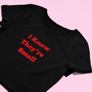 Puede incluir: Camiseta negra recortada con texto rojo que dice "I Know They're Small".