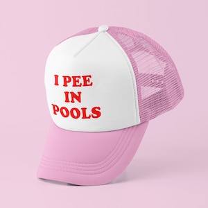 May include: A pink and white trucker hat with a white front panel and a pink mesh back. The front panel has the text "I PEE IN POOLS" in red letters.