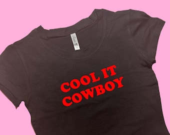 Pode incluir: Camiseta preta cropped com texto vermelho que diz "COOL IT COWBOY"