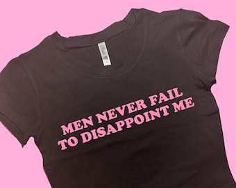May include: A black cropped t-shirt with pink text that reads "Men Never Fail To Disappoint Me."