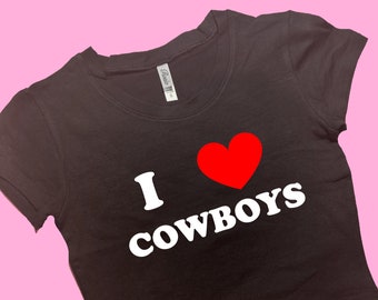 Pode incluir: Camiseta preta cropped com texto branco que diz "I love cowboys" e um coração vermelho.