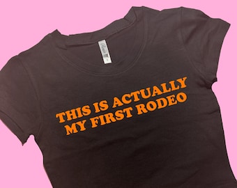 May include: Black cropped t-shirt with the text "This is actually my first rodeo" in orange.