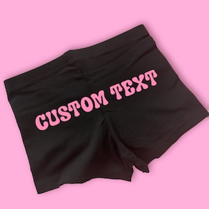 Könnte beinhalten: Schwarze Shorts mit dem Text "CUSTOM TEXT" in rosa Buchstaben.